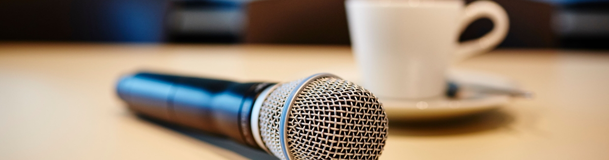 Lehdistötilaisuustunnelma: mikrofoni ja kuppi kahvia pöydällä.