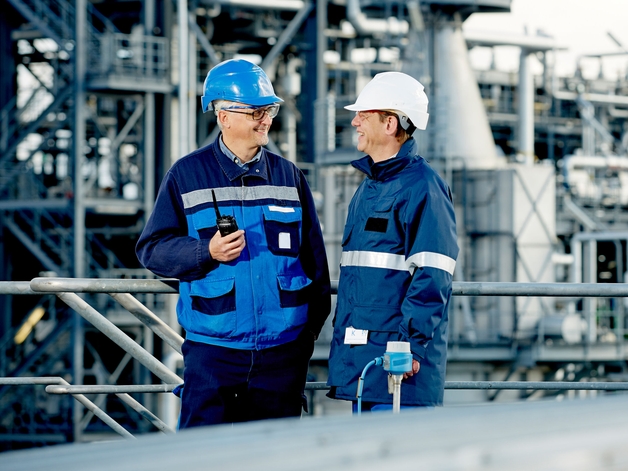 Two engineers work standing in a refinery.