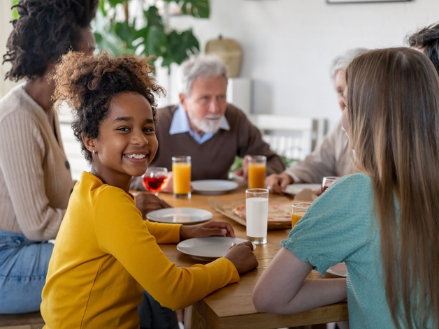 Young girl smiling into the camera while sitting at the dining table with her family.